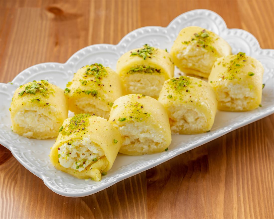 Halawet el jibn, cheese rolls topped with pistachio, on a white tray